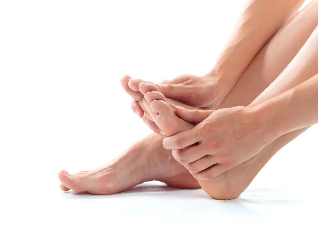 Person holding the ball of a bare foot with both hands, with the other foot resting on a white surface
